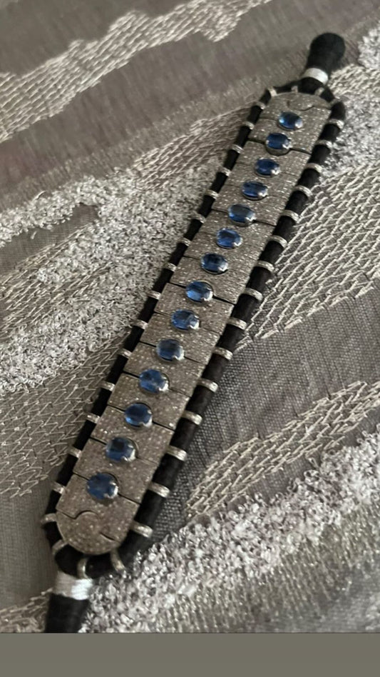 Detailed view of a unique artisan bracelet showcasing lustrous silver, oval blue kyanite gems, and small diamonds, set on a distinct hand-stitched fabric foundation.