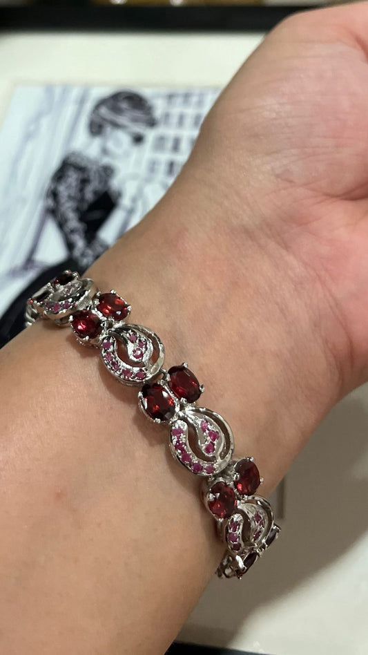 Elegant sterling silver bracelet featuring multiple rich red gemstones, including rubies and garnets, in a flowing, decorative pattern on a wrist.