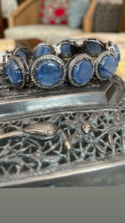 Top-down view of a luxurious sterling silver bracelet featuring a large, oval cabochon deep blue Kyanite stone as the centerpiece, surrounded by a sparkling halo of small diamonds