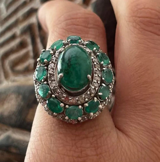 Close-up of a Victorian-style sterling silver ring featuring a large, smooth 6.08 carat Zambian emerald cabochon as the centerpiece, surrounded by sparkling diamonds.