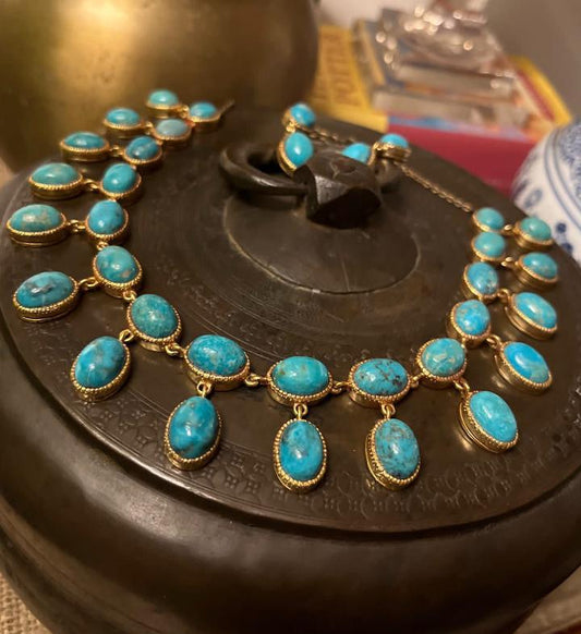 Close-up of a handmade gold-plated necklace featuring numerous oval and round turquoise cabochon stones, each individually set, arranged in a multi-strand or bib style.