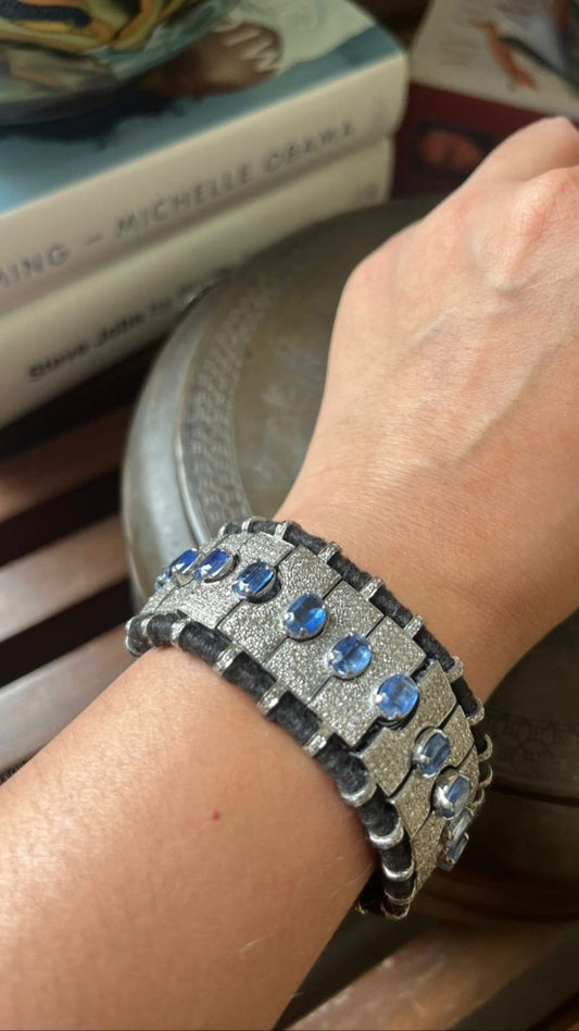 Close-up of a luxurious handmade sterling silver bracelet featuring multiple rectangular segments, each studded with faceted deep blue kyanite stones and sparkling melee diamonds, all meticulously stitched onto a dark, intricate fabric base.