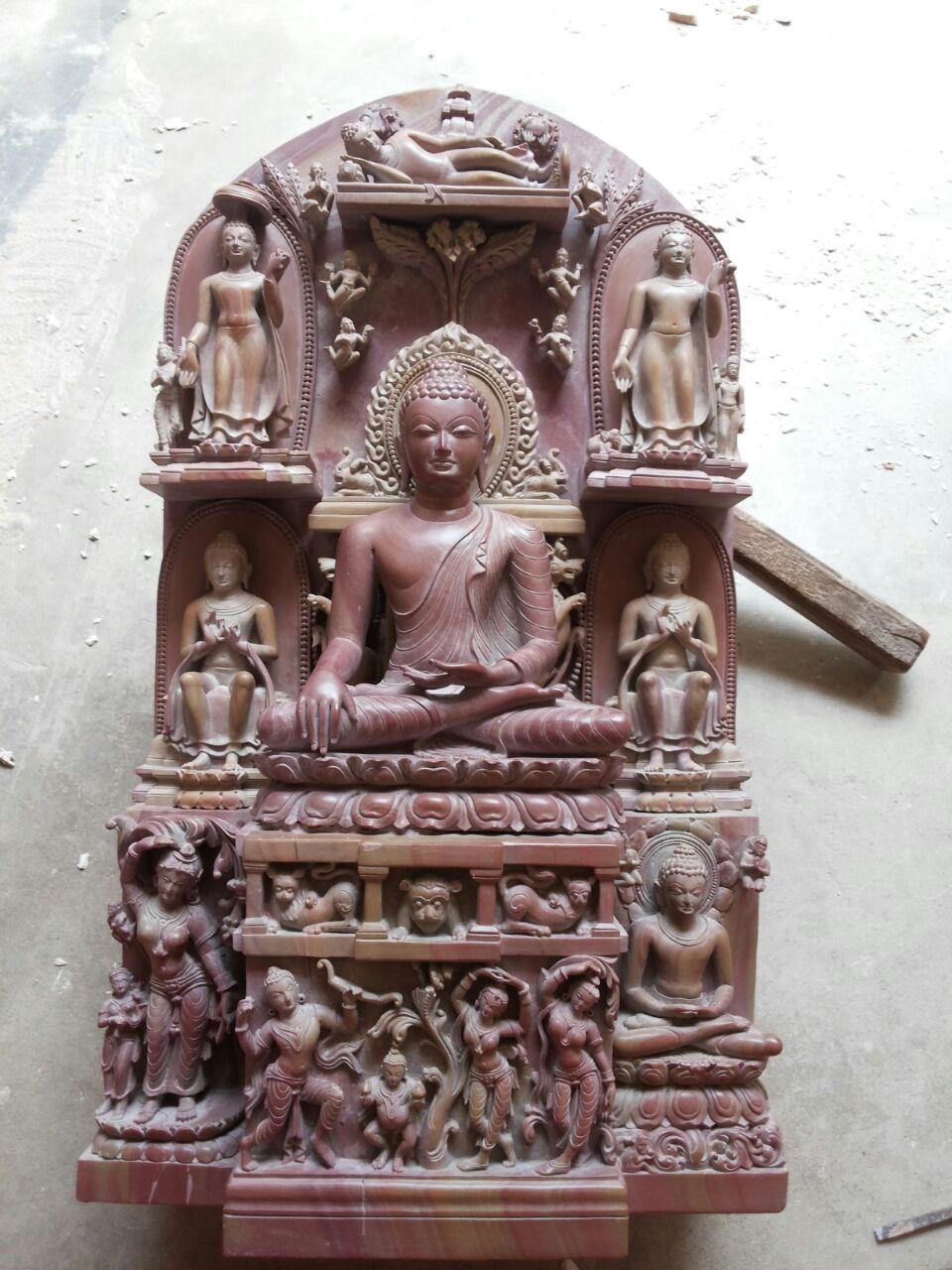 Hand-carved red stone Buddha statue with detailed carvings of scenes from the life of the Buddha